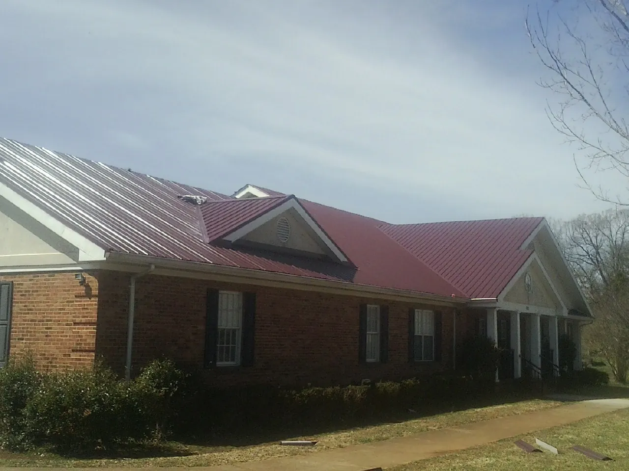 Red metal roof with gabled entries on a long brick building, from a Hail Damage Roof Repair job in Cocolalla