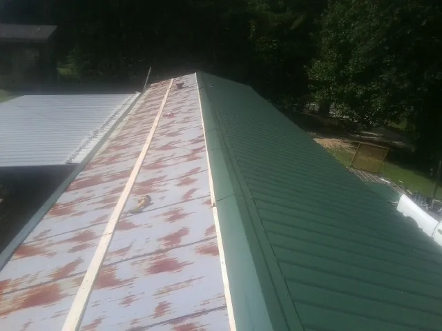 Old rusted panels beside newly installed green metal roofing — Wind Damage Roof Repair by Roofing Brothers in Cocolalla