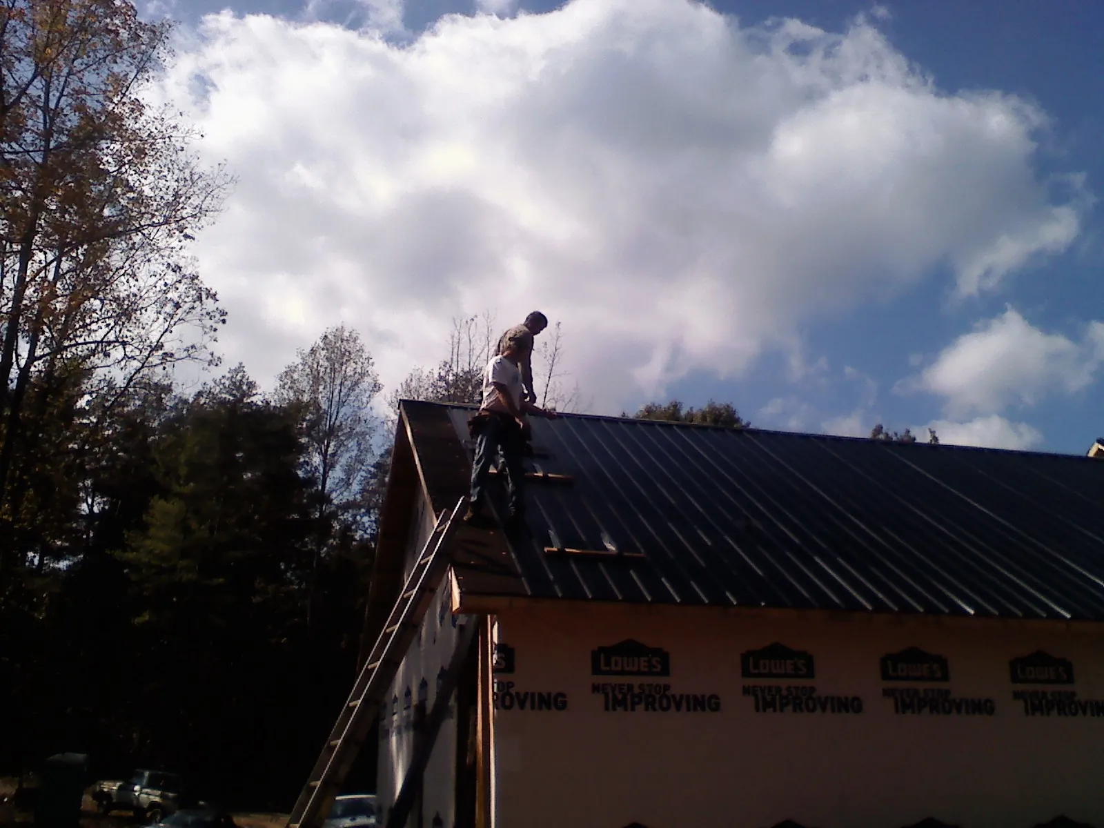 Roofer fastening dark metal panels high against a cloudy sky, from a Roof Inspection job in Cocolalla
